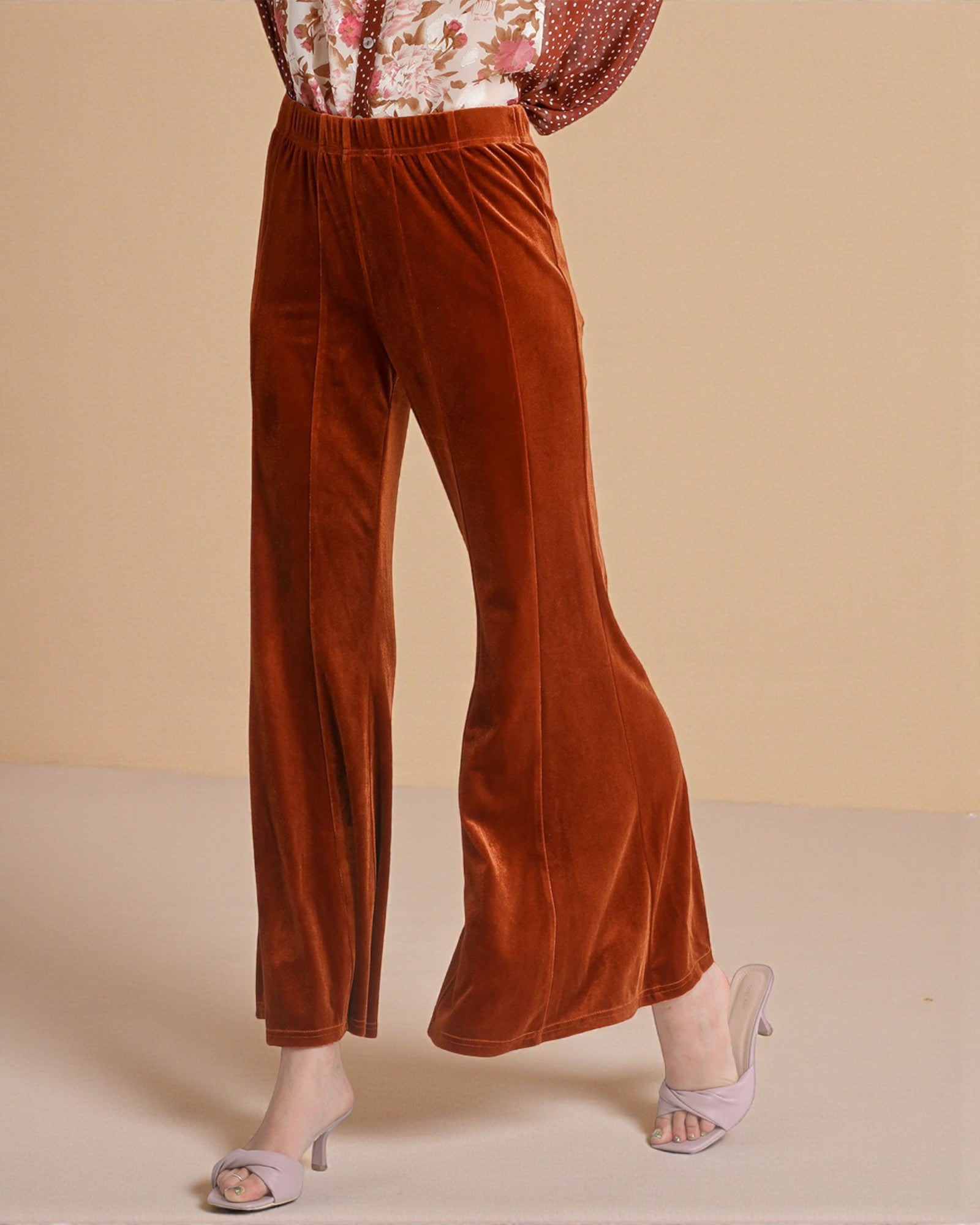 Brown velvet pants worn by a person on a beige background