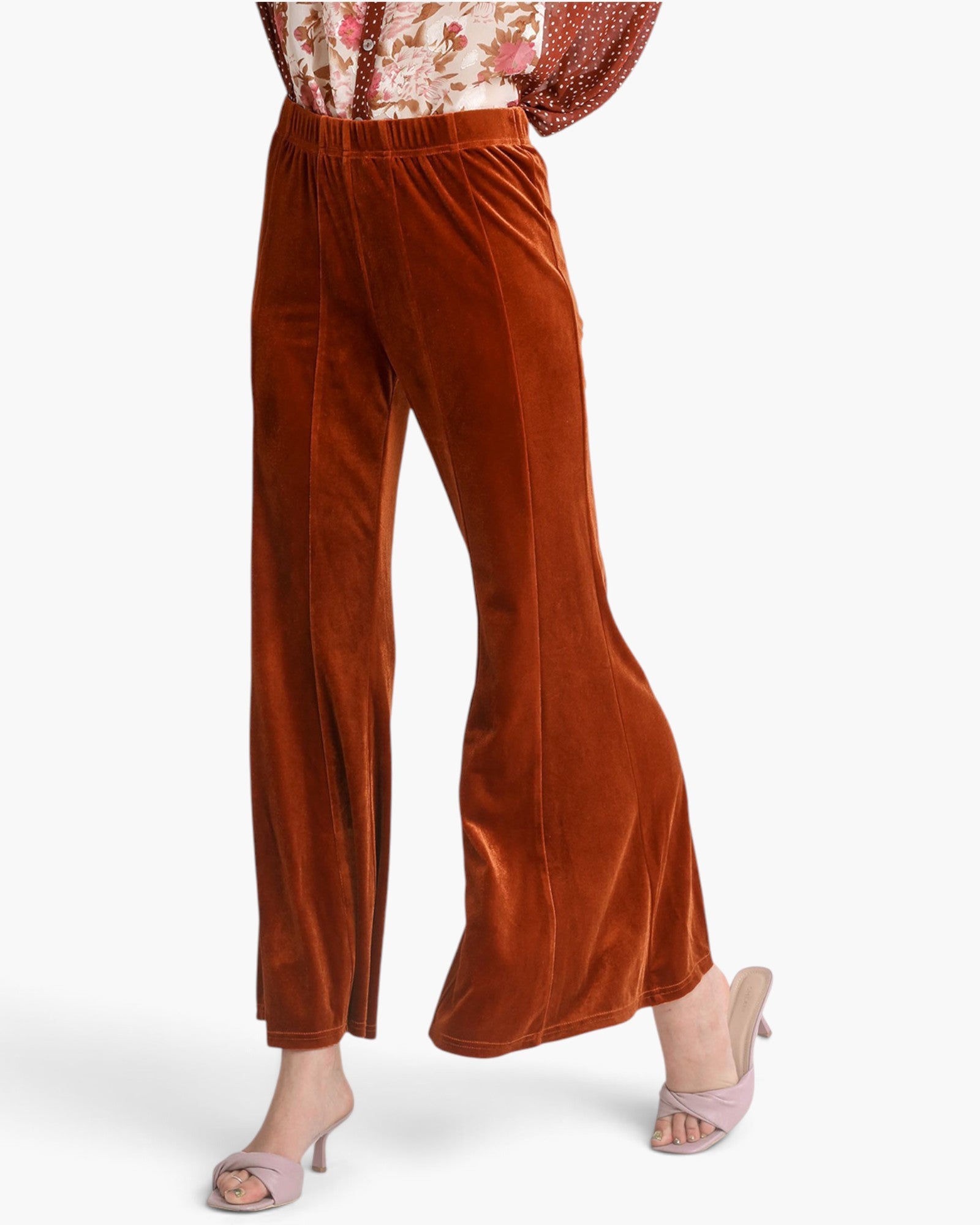 A model wearing rust-brown velvet wide-leg pants with a matching patterned top and light pink heeled sandals, shown from the waist down against a light gray studio background.