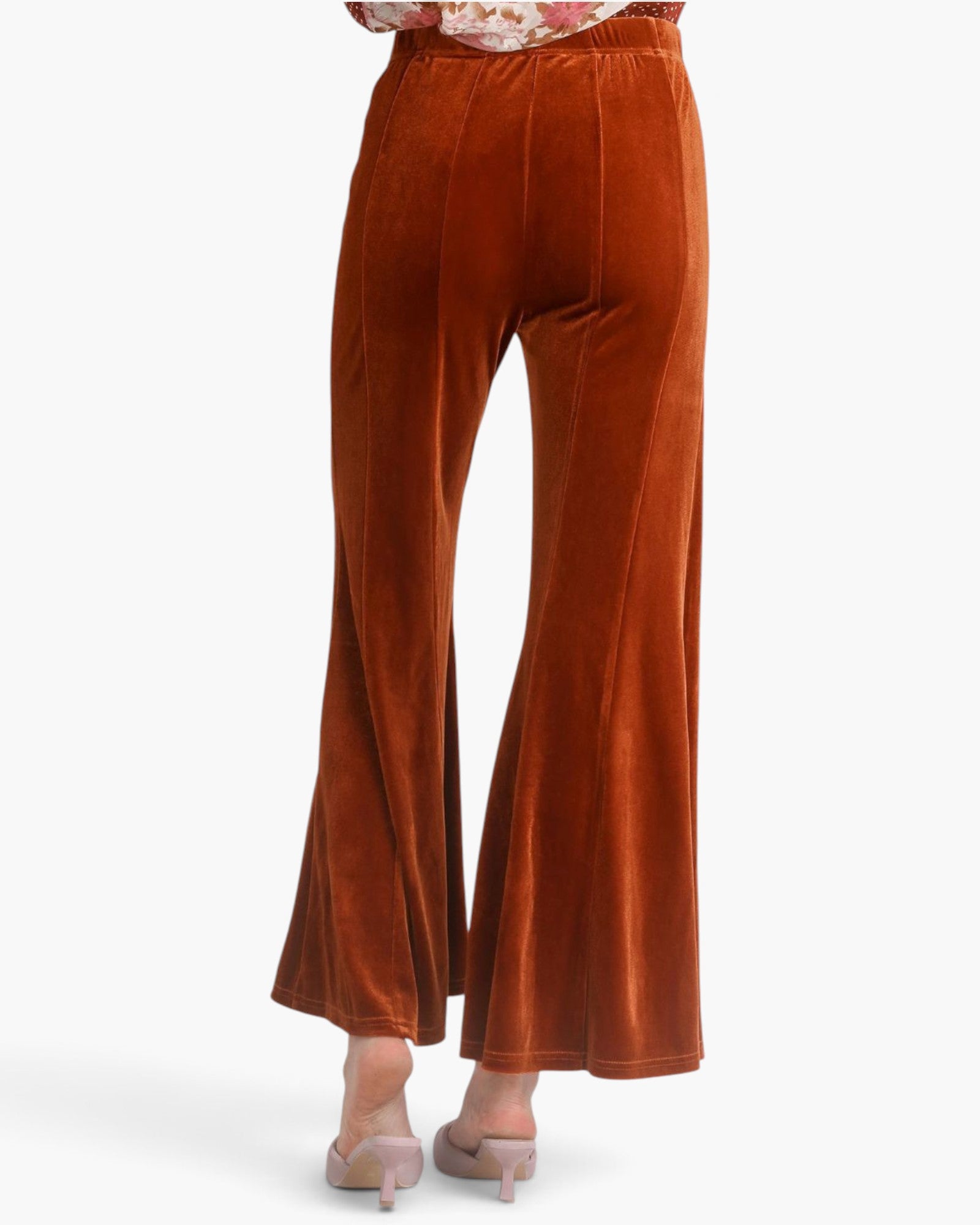 A pair of rust-orange velvet wide-leg pants shown on a model from the back, paired with nude heels against a clean white background.
