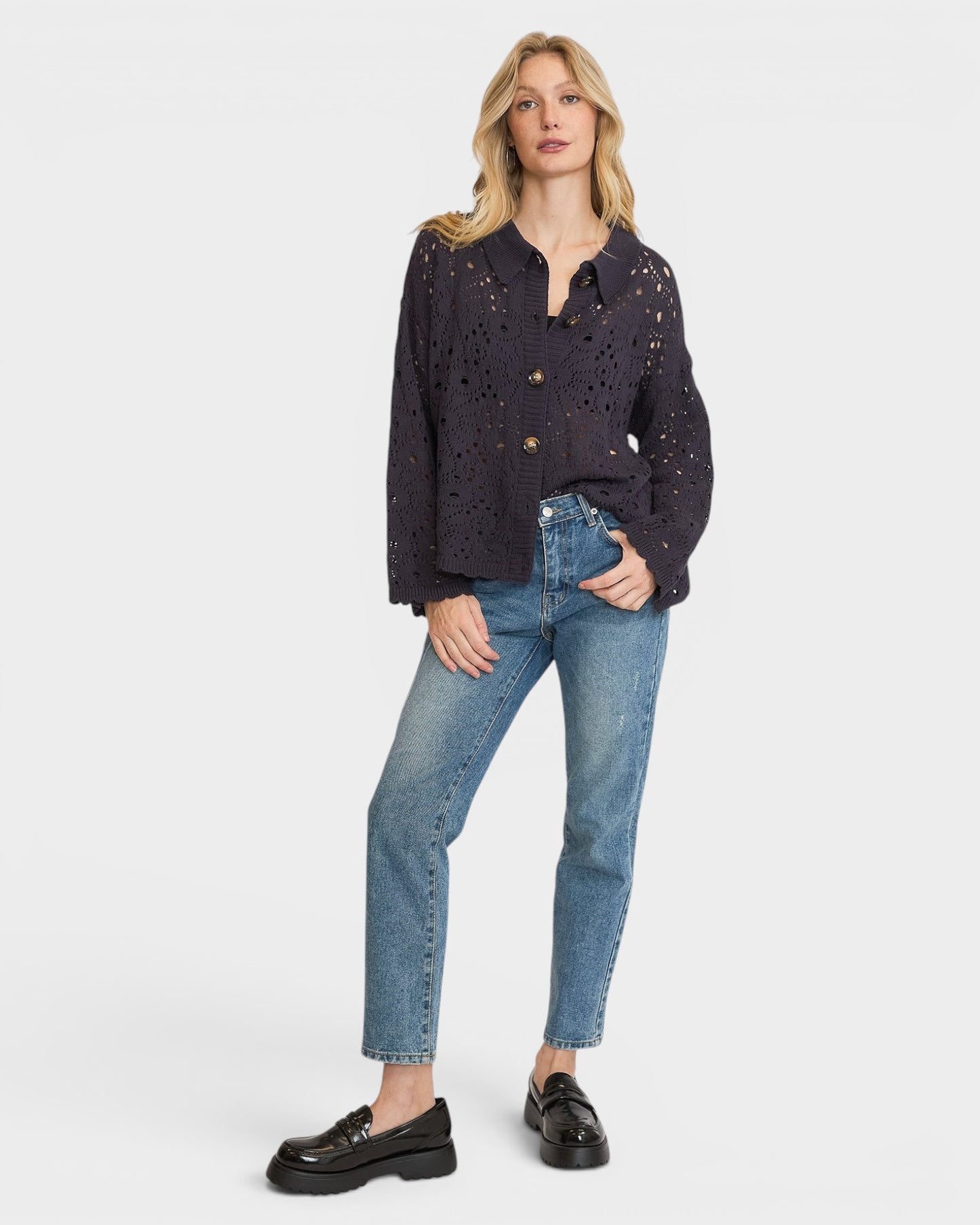 Woman wearing a dark navy blouse with lace details and blue jeans on a white background
