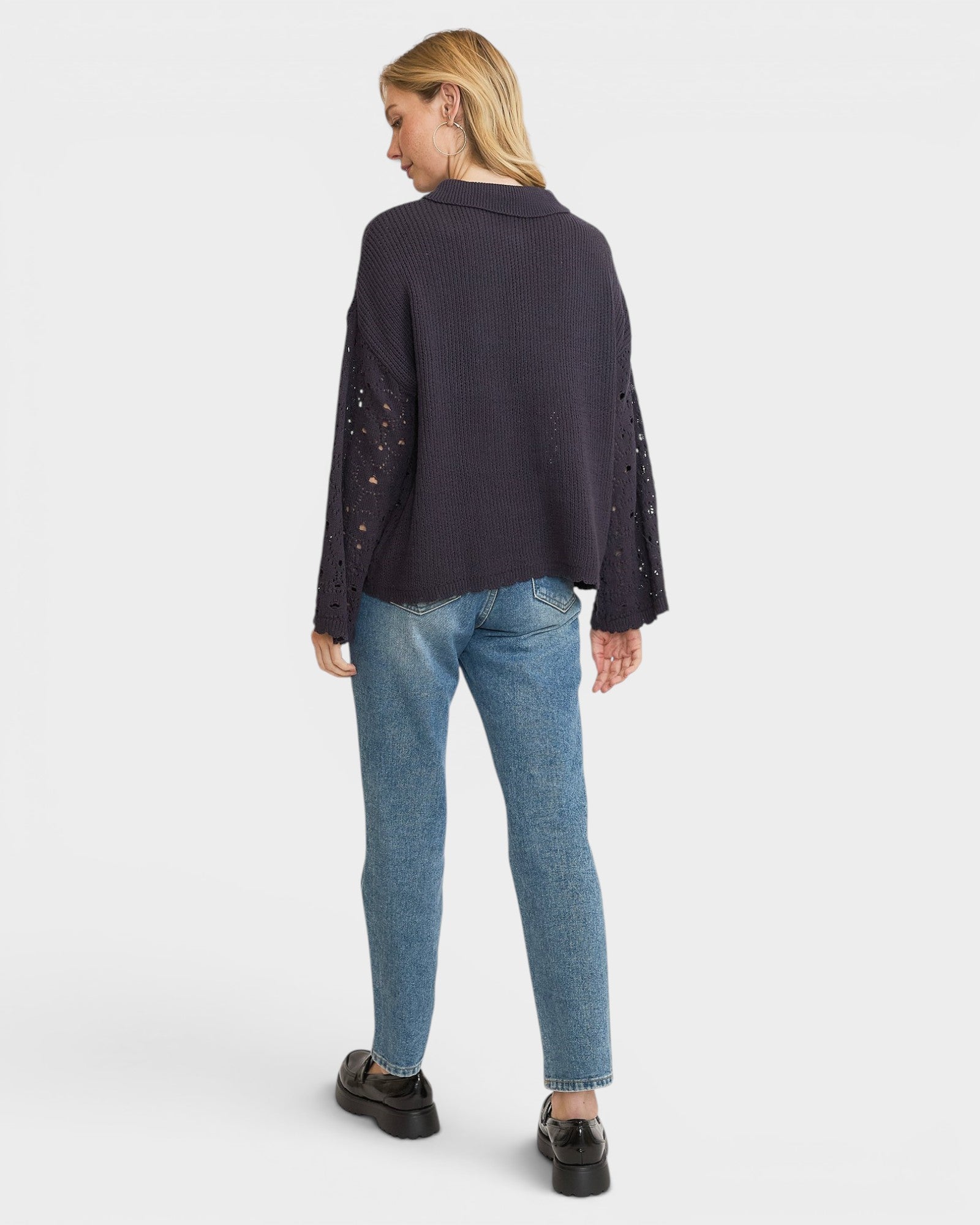 Person wearing a dark blue cardigan with lace sleeves and light blue jeans on a white background