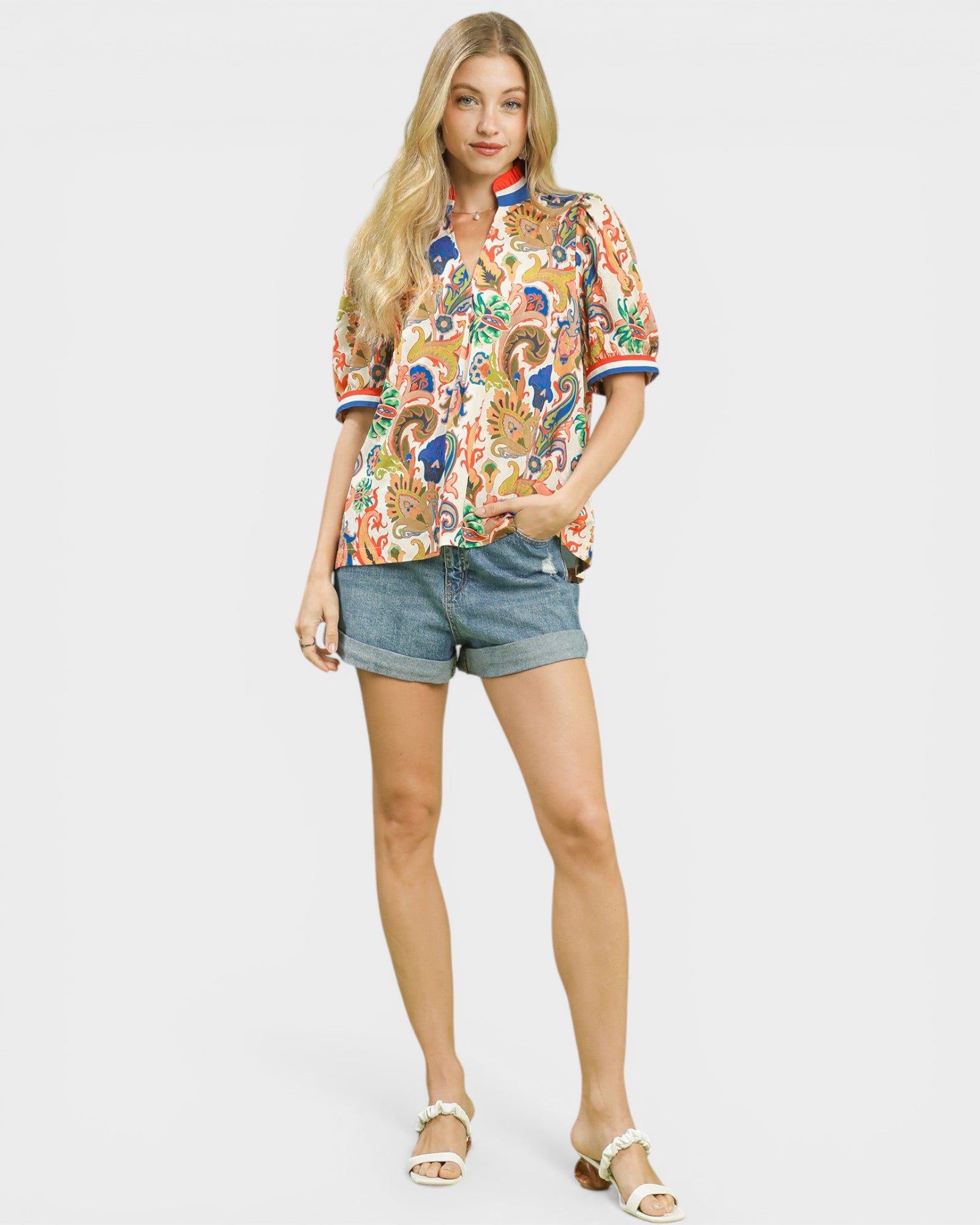 Woman wearing a colorful floral blouse and denim shorts on a white background