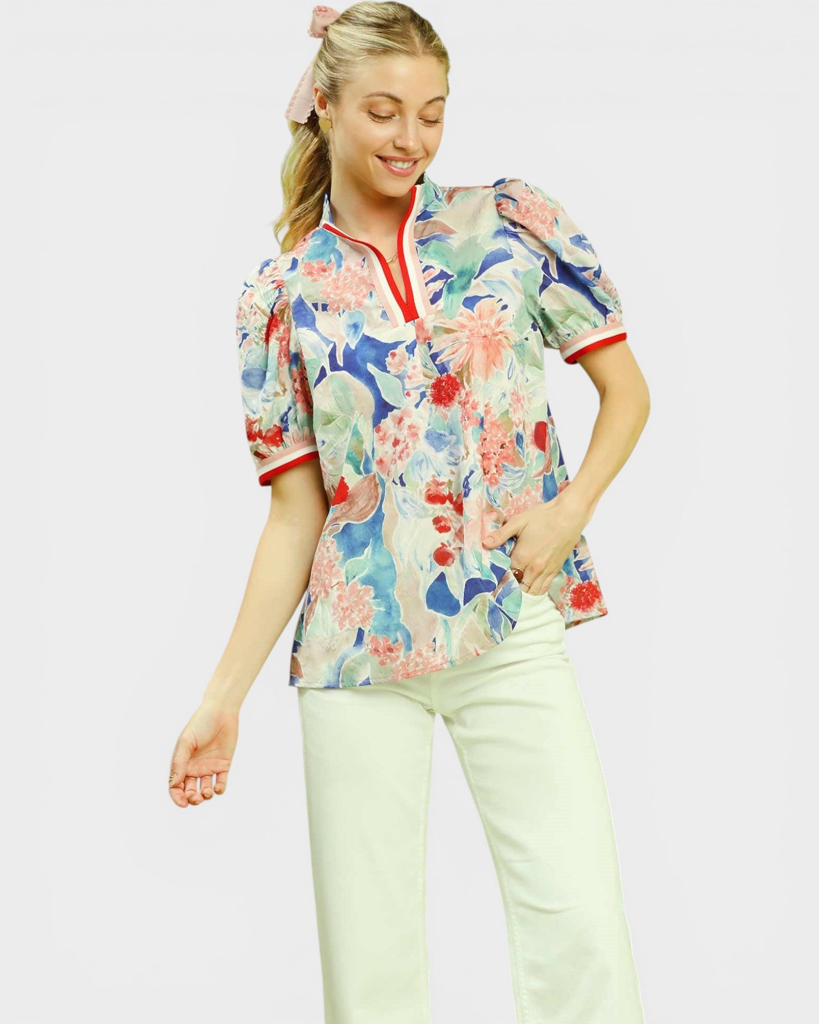 Woman wearing a colorful floral blouse with white pants on a light gray background