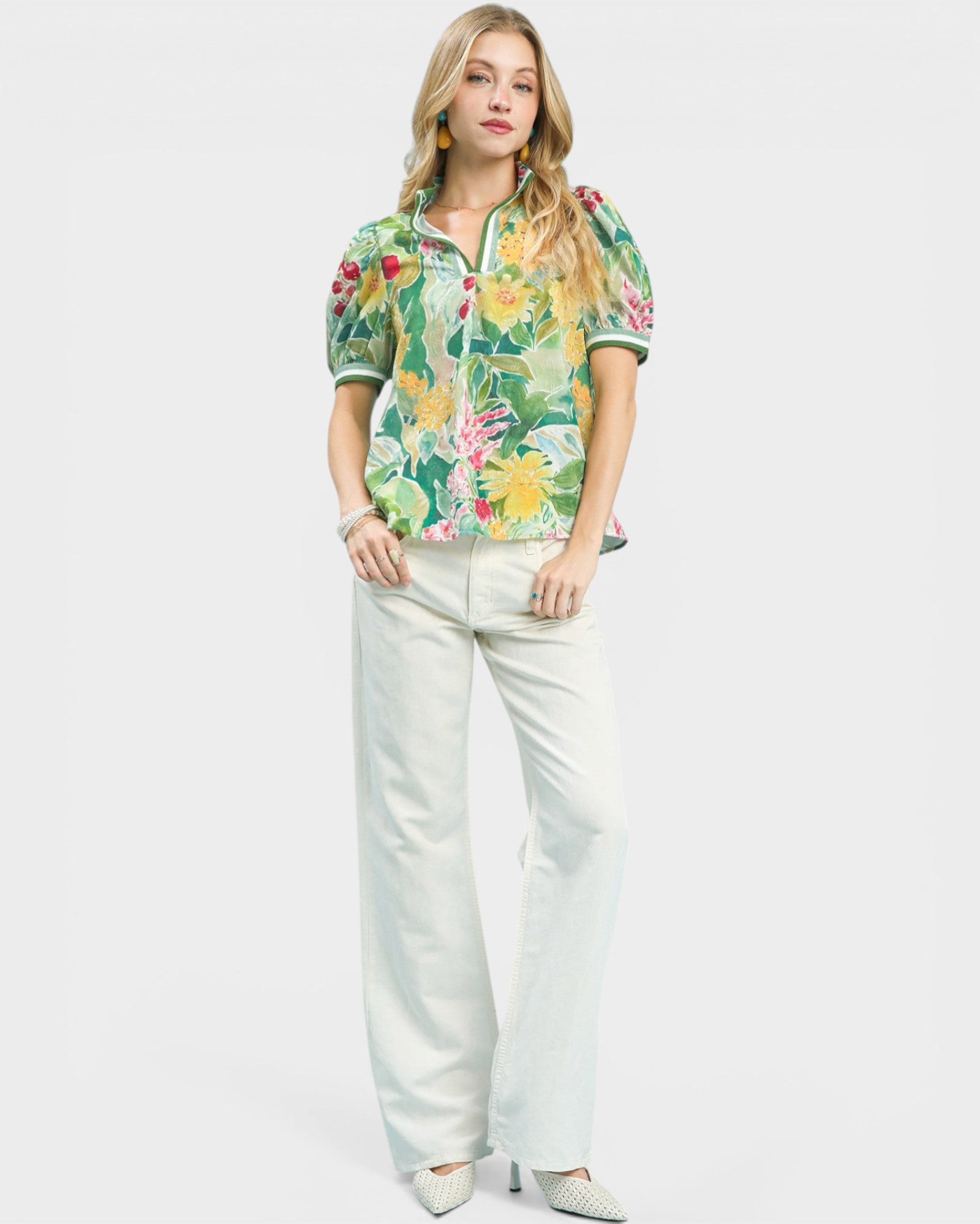 Woman wearing a floral blouse and white pants on a plain background