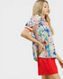 Woman wearing a colorful floral shirt and red shorts on a white background
