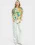 Woman wearing a floral blouse and white pants on a plain background