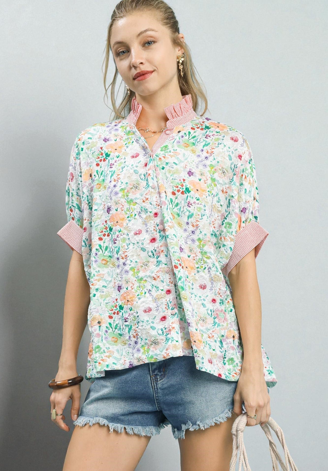 Woman wearing a floral blouse with pink accents and denim shorts on a gray background