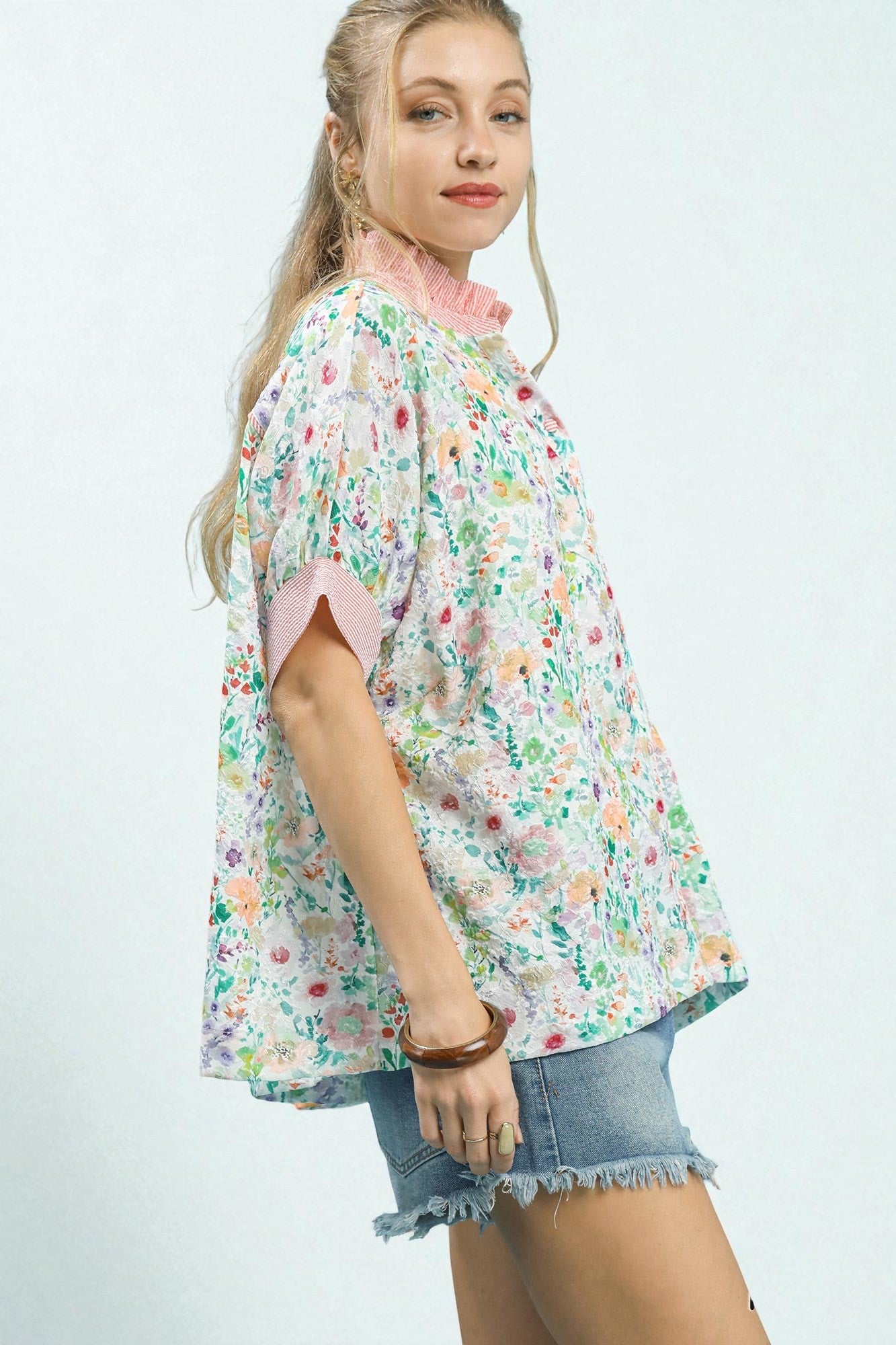 Woman wearing a floral blouse and denim shorts on a white background