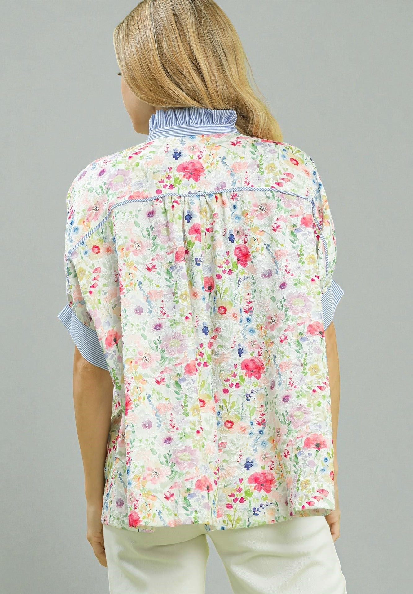 Person wearing a floral vest over a light blue shirt on a gray background