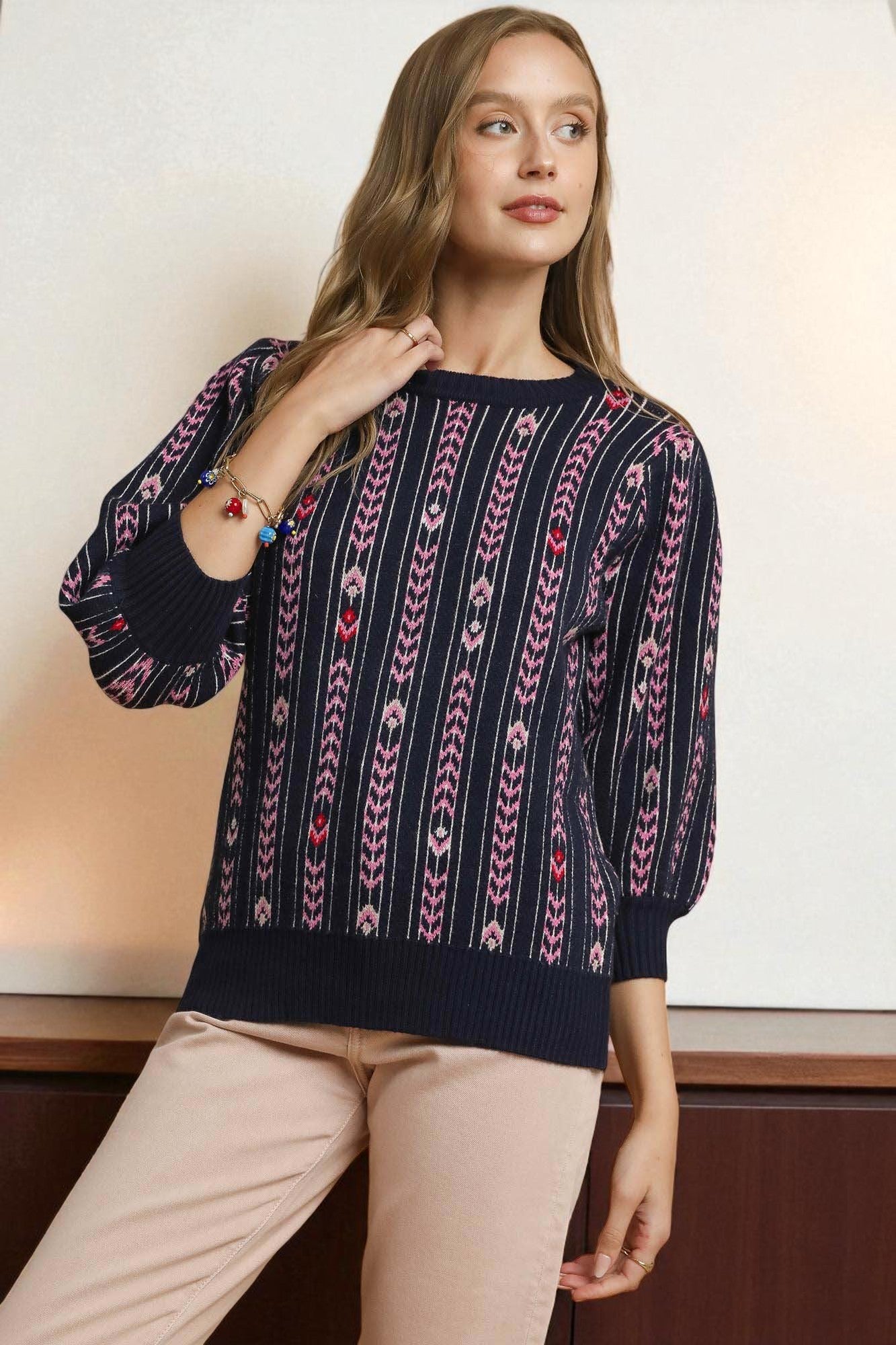 Woman wearing a navy sweater with a pattern, standing against a neutral background