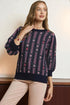 Woman wearing a navy sweater with a pattern, standing against a neutral background