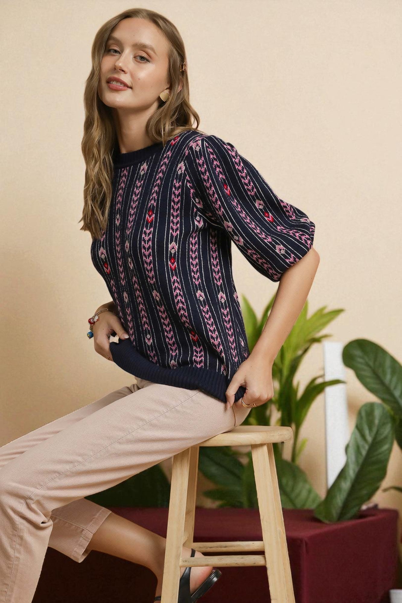 Woman sitting on a stool wearing a patterned top with a beige background