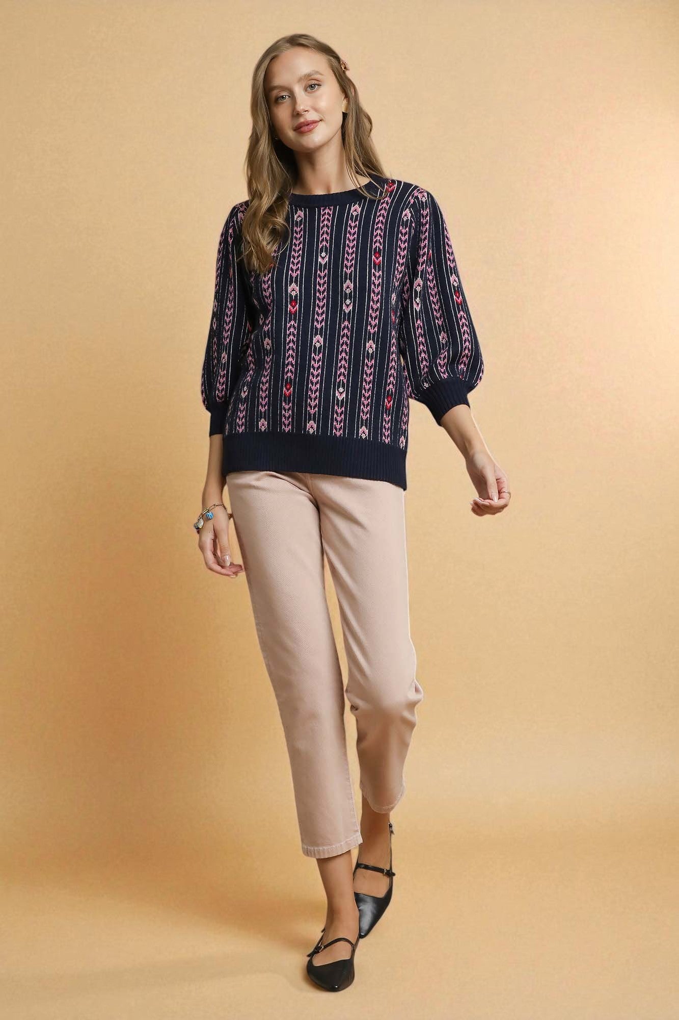 Woman wearing a patterned top and beige pants on a beige background