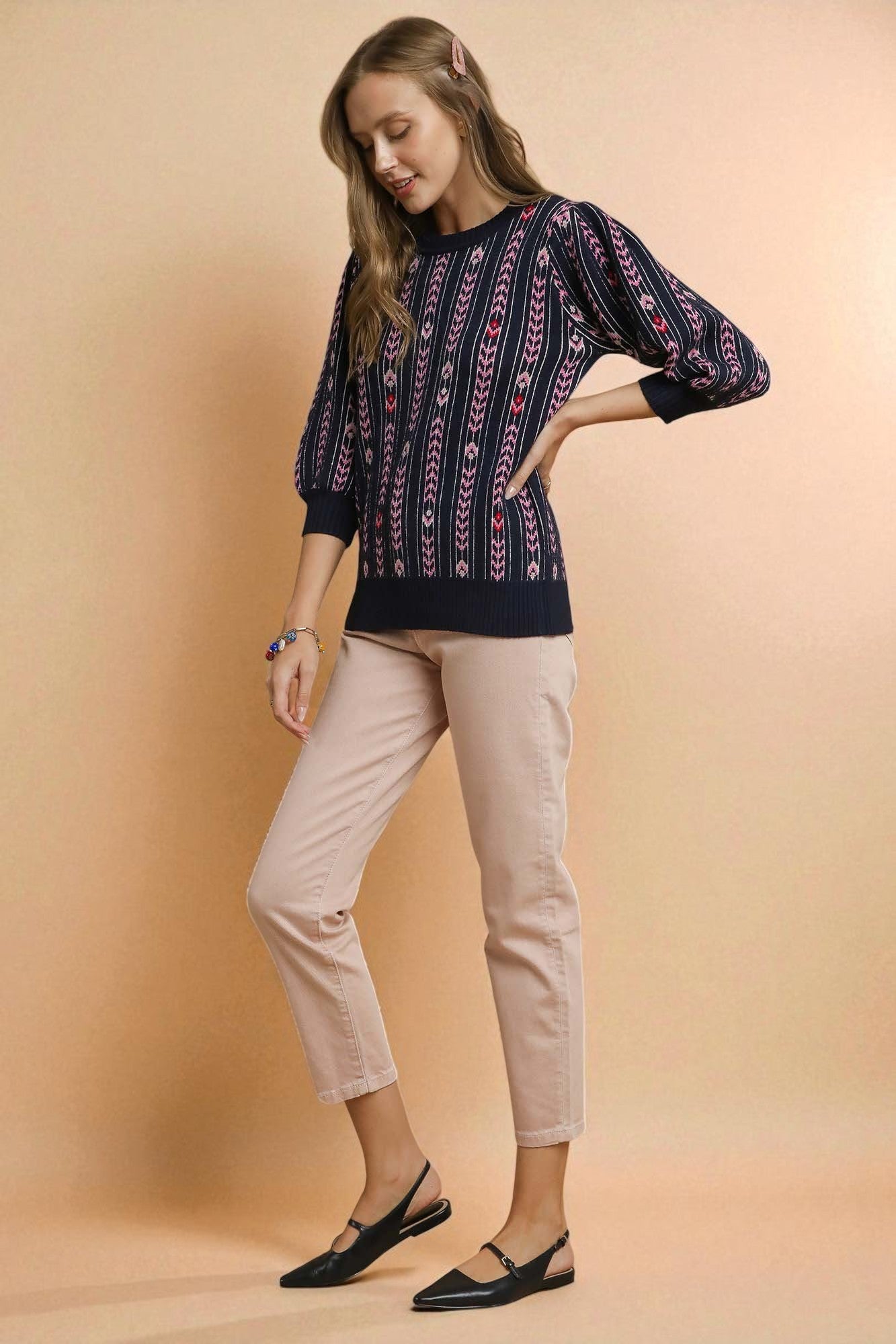 Woman wearing a patterned navy sweater and beige pants on a beige background