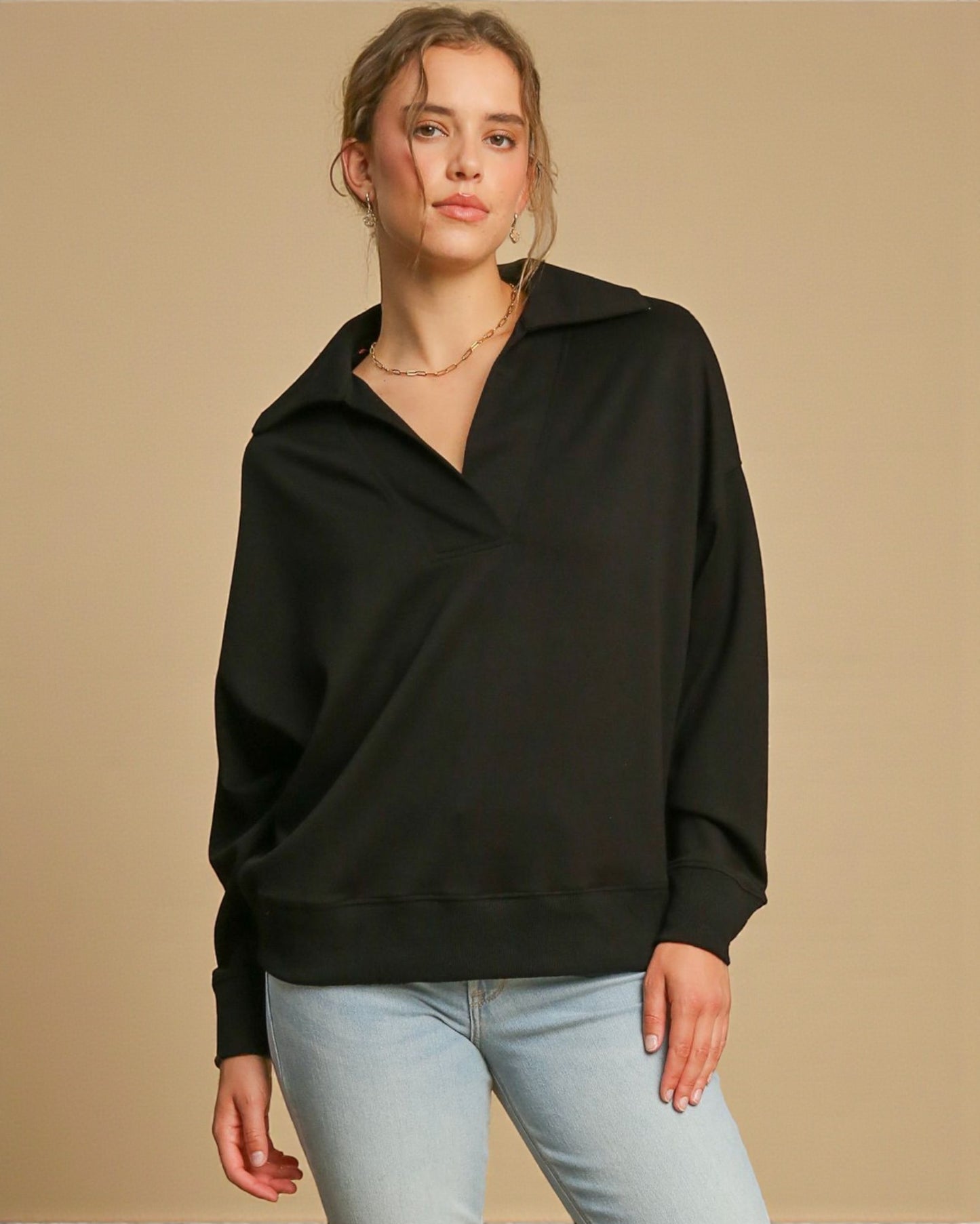 Woman wearing a black sweater and light blue jeans against a beige background