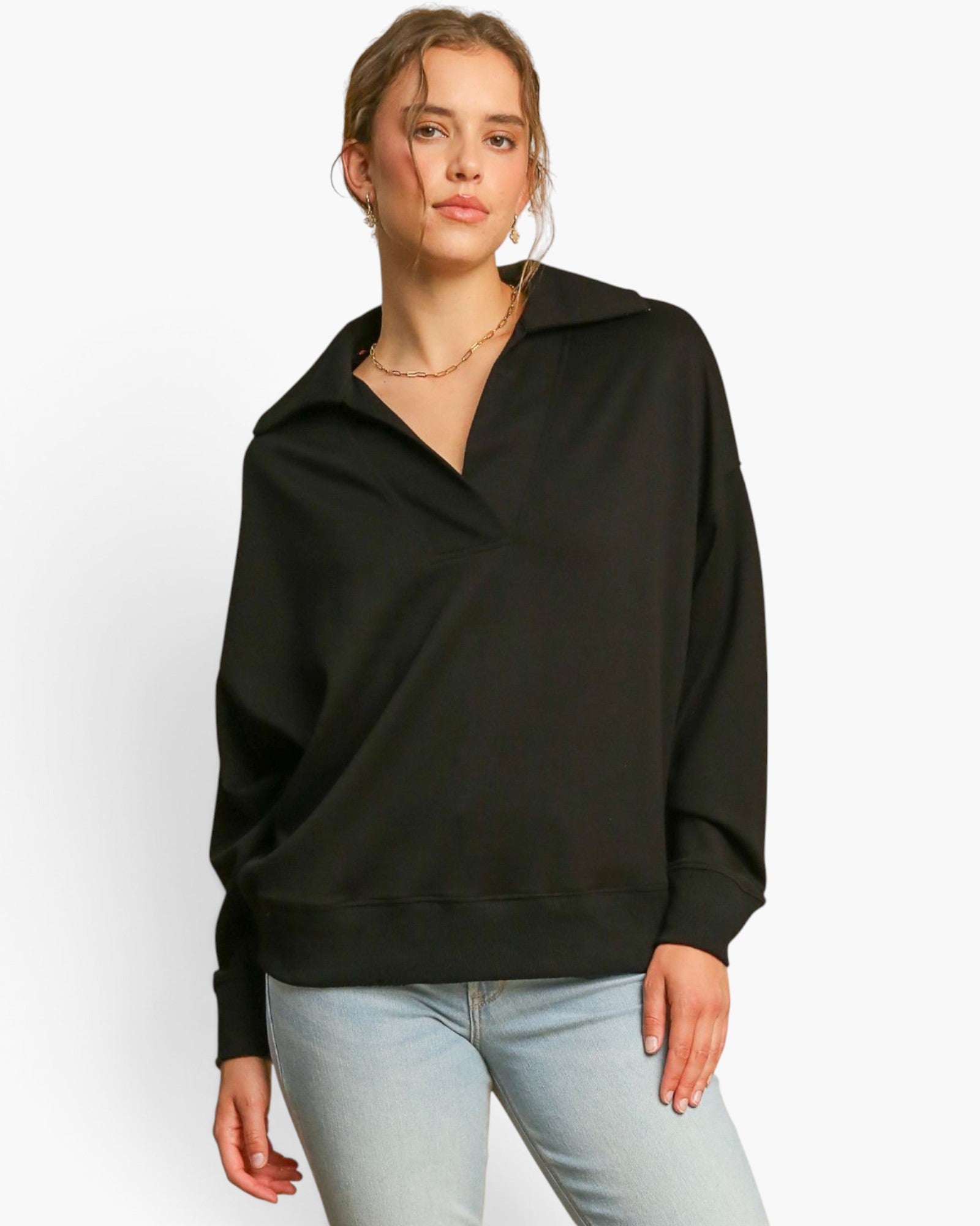 A woman modeling a black oversized long-sleeve pullover sweatshirt with a split collar, paired with light blue jeans, against a plain white studio background.