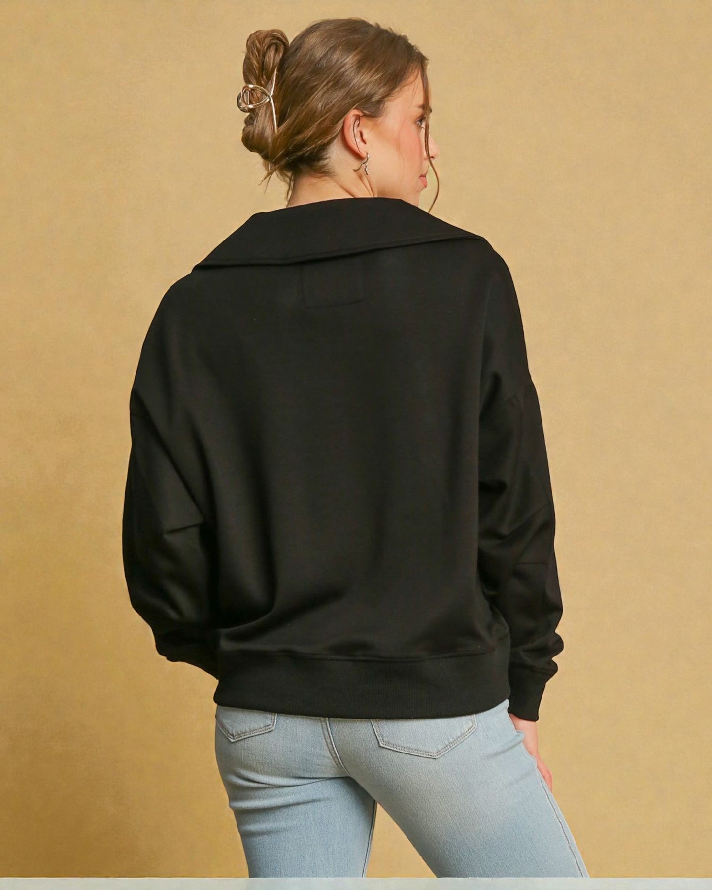 Person wearing a black sweater and light blue jeans against a beige background