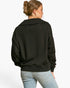 A woman shown from the back wearing a black long-sleeve cropped sweatshirt and light blue jeans against a plain white studio background.