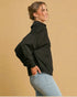 Woman wearing a black jacket and light blue jeans against a beige background