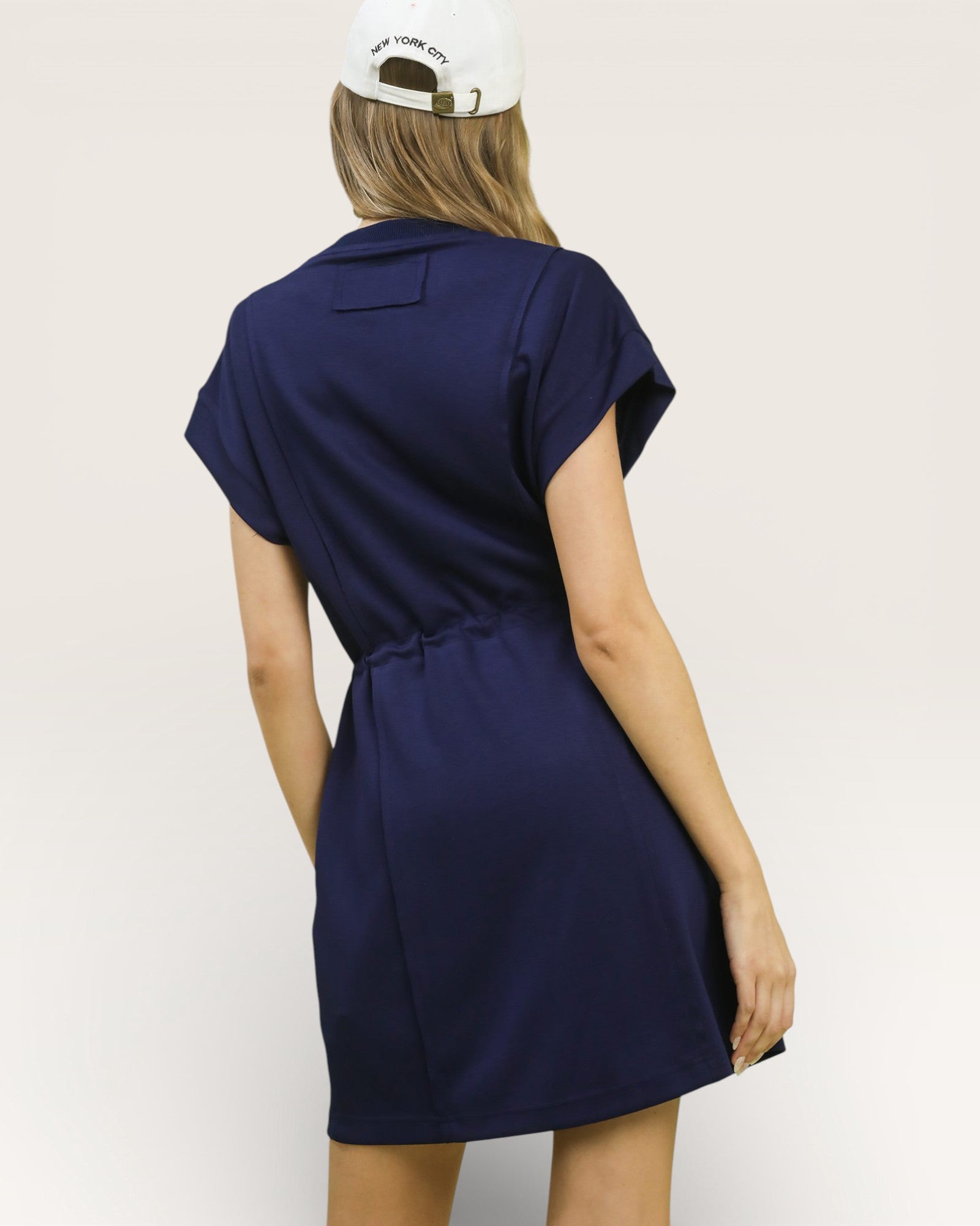 Person wearing a navy blue dress with a white cap on a light gray background