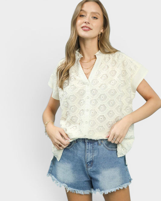 Woman wearing a white lace top and denim shorts on a plain background