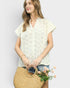Woman holding a straw bag with flowers, wearing a light-colored blouse against a plain background