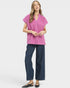 Woman wearing a pink blouse with lace details and blue pants on a white background