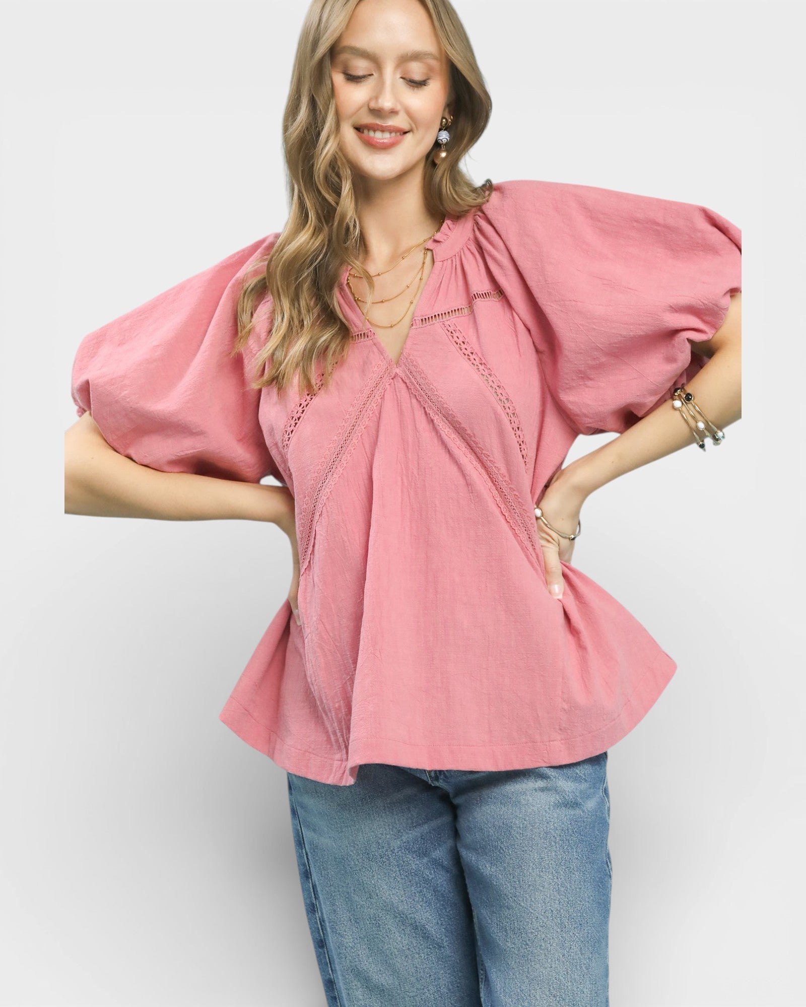 Woman wearing a pink blouse with puffed sleeves and blue jeans on a white background