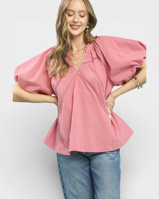 Woman wearing a pink blouse with puffed sleeves and blue jeans on a white background