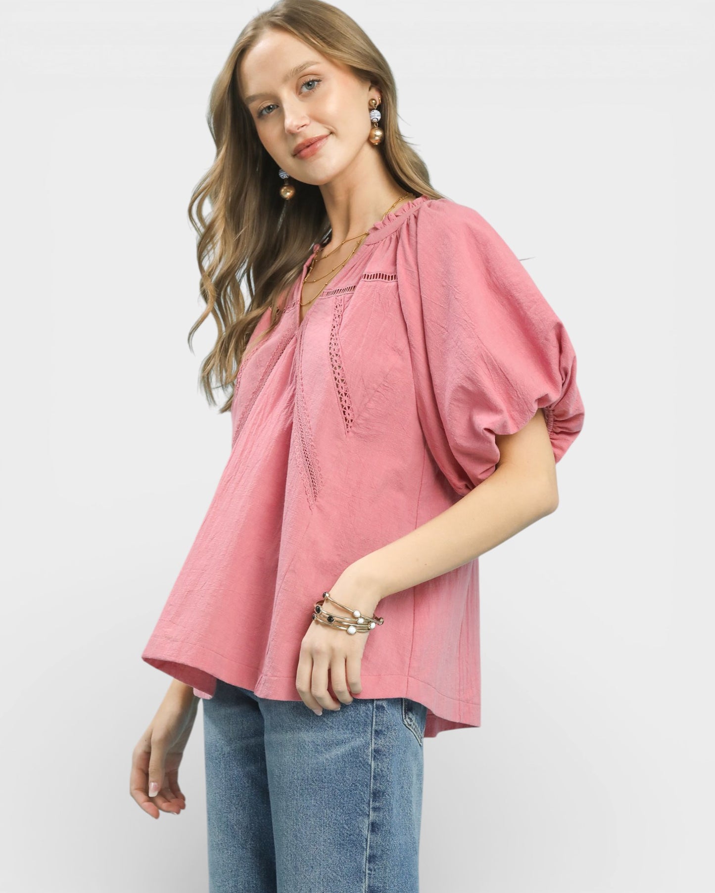 Woman wearing a pink blouse with ruffled sleeves and blue jeans on a white background