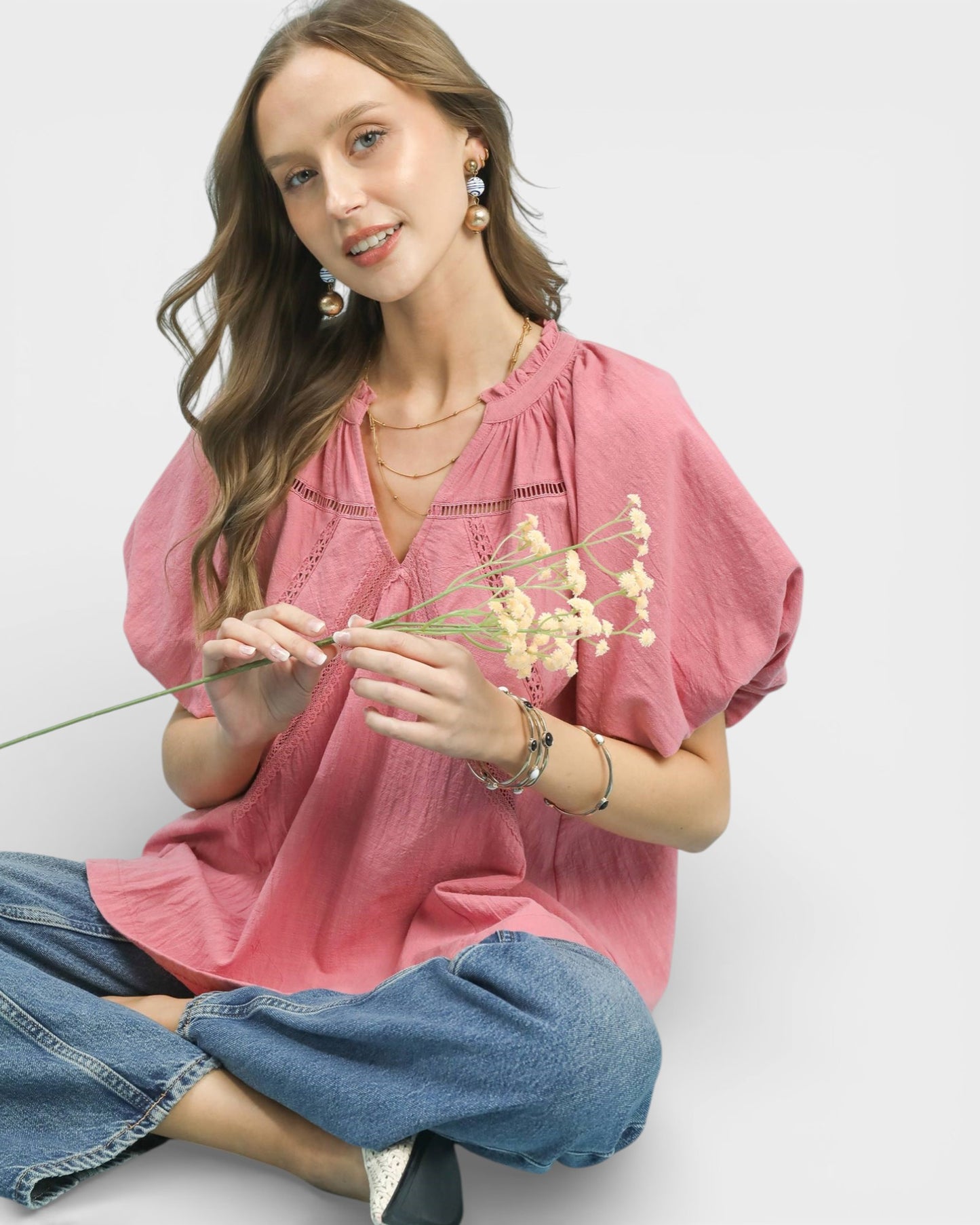 Woman wearing a pink blouse and blue jeans holding flowers against a white background