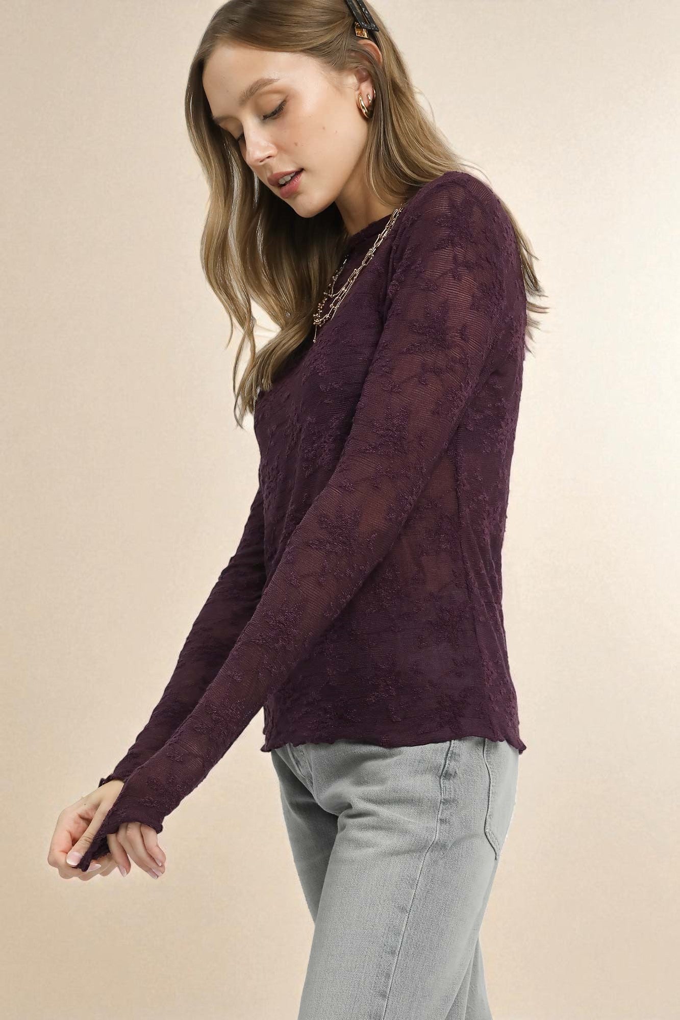 Woman wearing a dark purple long-sleeve top with a subtle pattern on a beige background