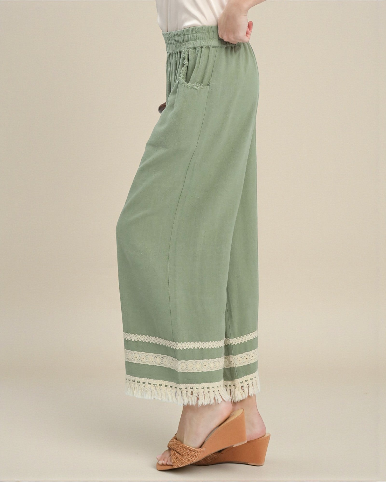 Green pants with white lace trim worn by a person on a beige background