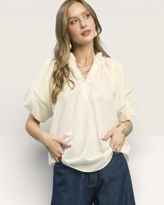 Woman wearing a cream blouse with lace details and blue jeans on a light gray background
