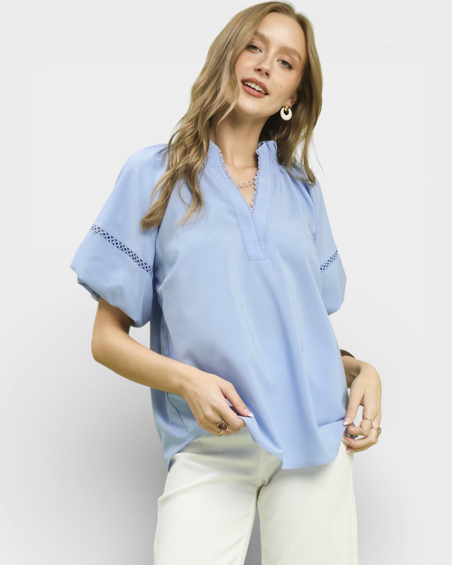 Woman wearing a light blue blouse with white pants on a plain background