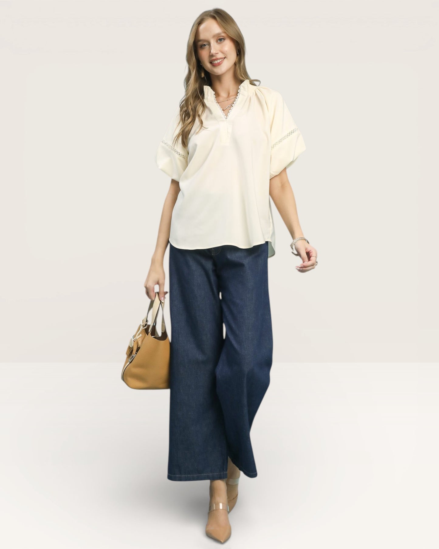 Woman wearing a white blouse and blue jeans with a tan handbag on a white background