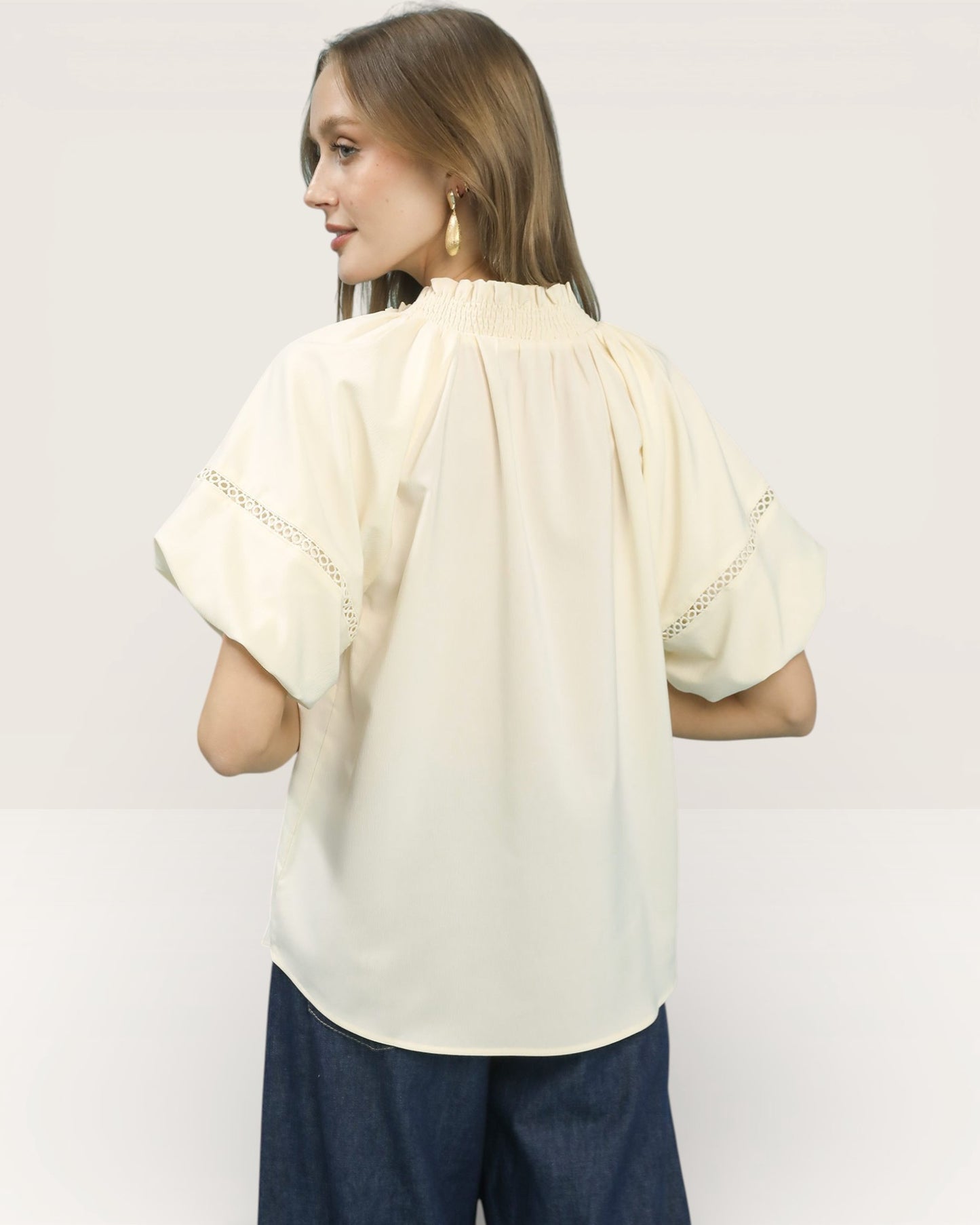 Woman wearing a cream blouse with short sleeves and blue pants on a white background