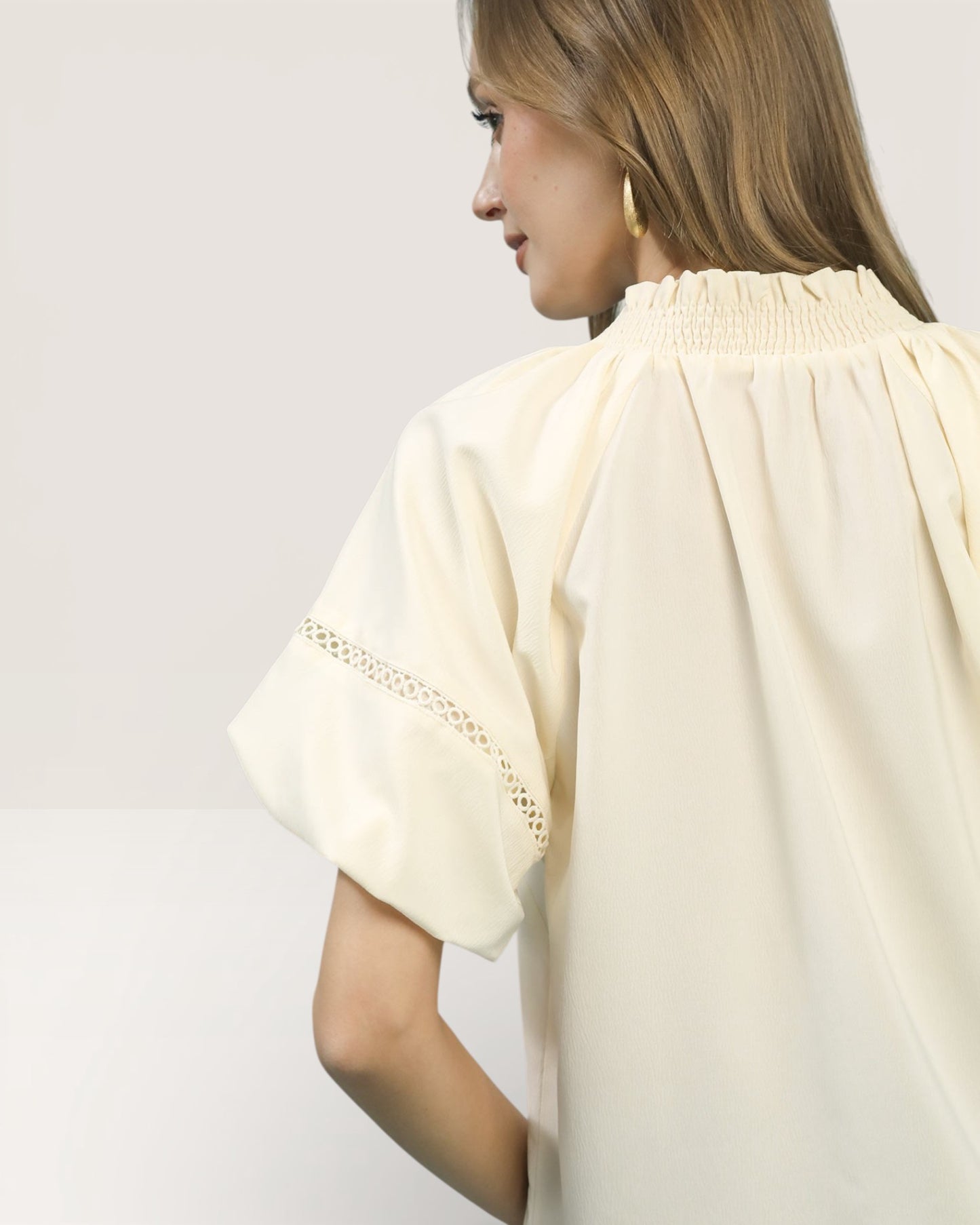 Woman wearing a light yellow blouse with lace sleeves on a plain background