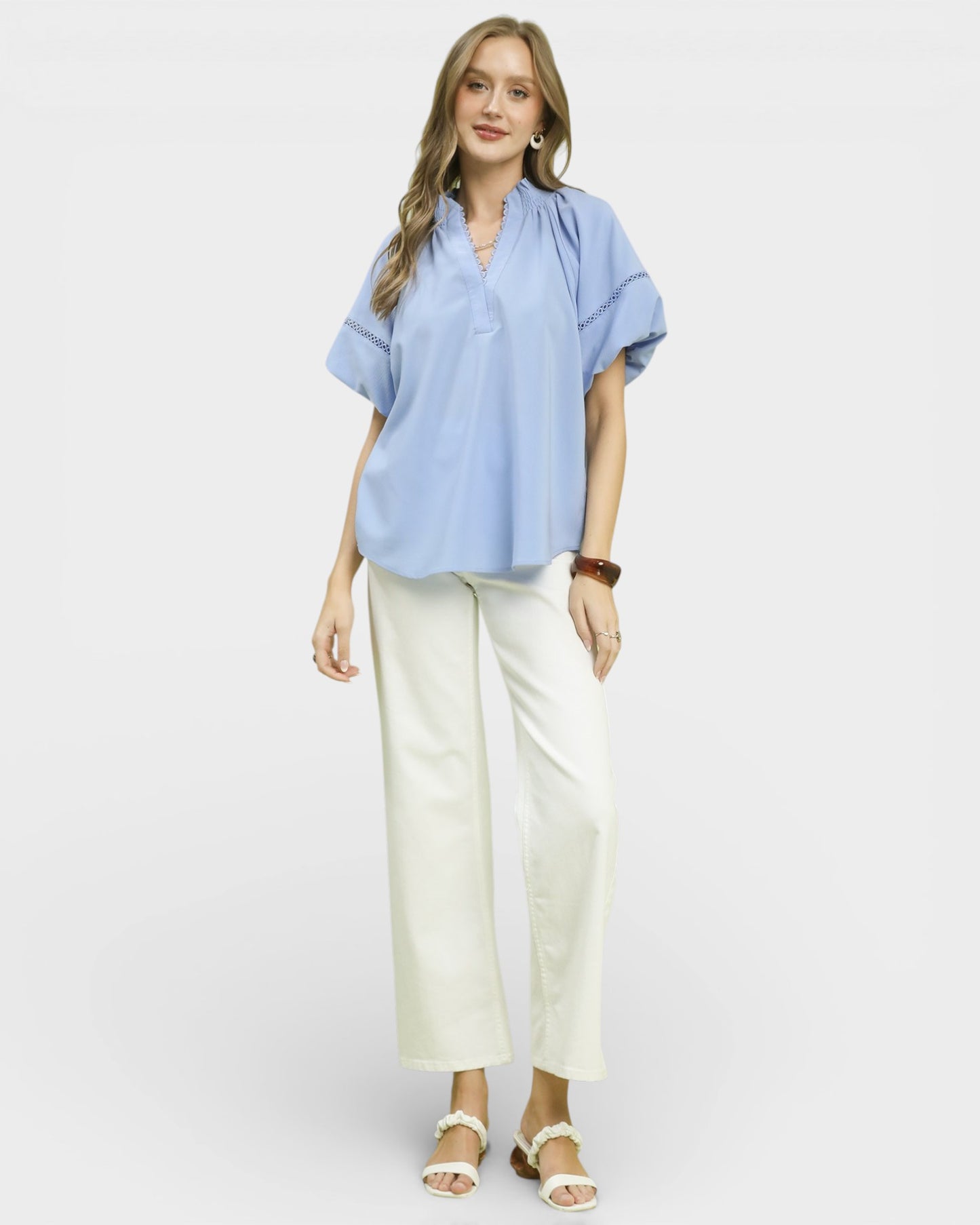 Woman wearing a light blue blouse and white pants on a plain background