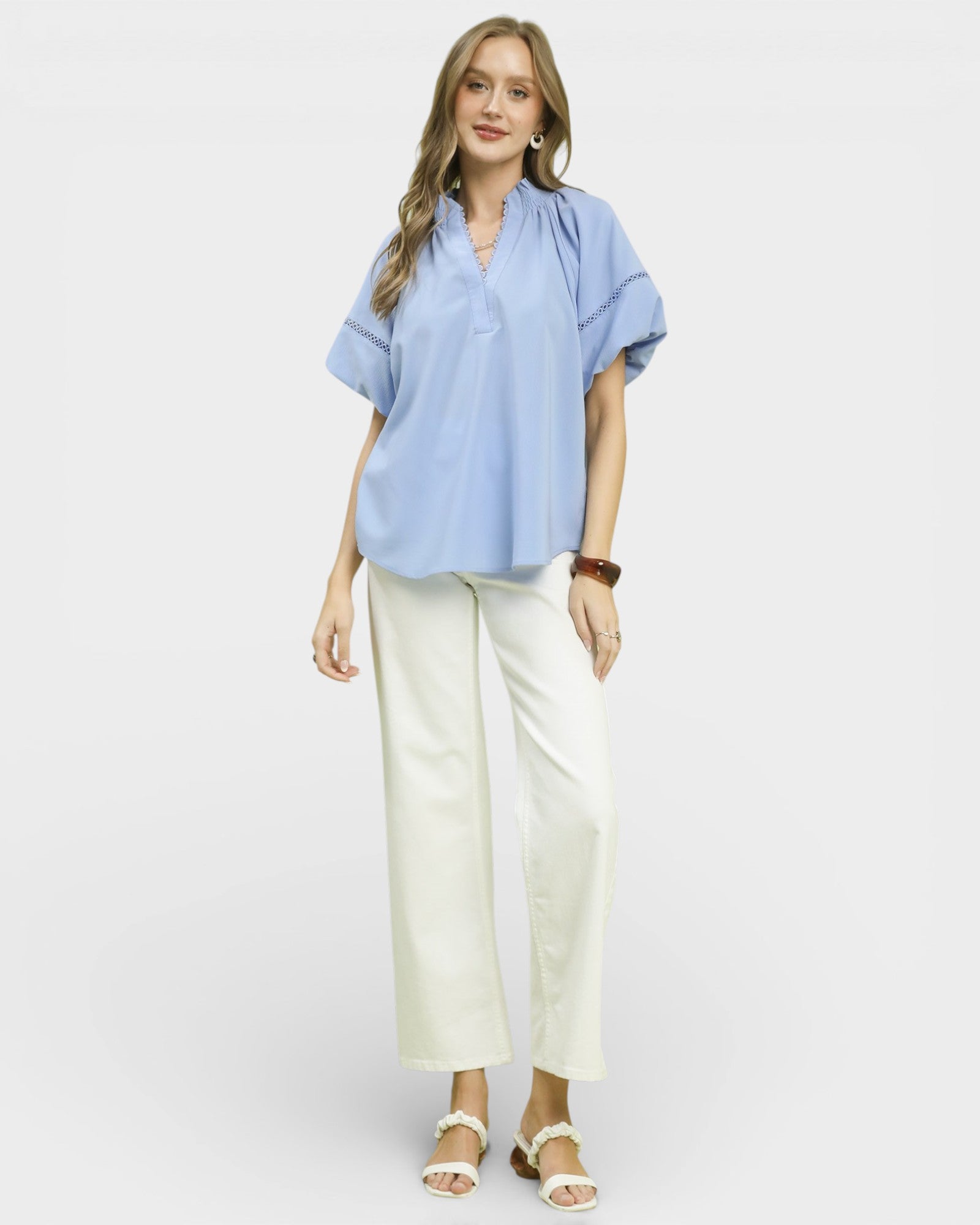 Woman wearing a light blue blouse and white pants on a plain background