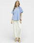 Woman wearing a light blue blouse and white pants on a plain background