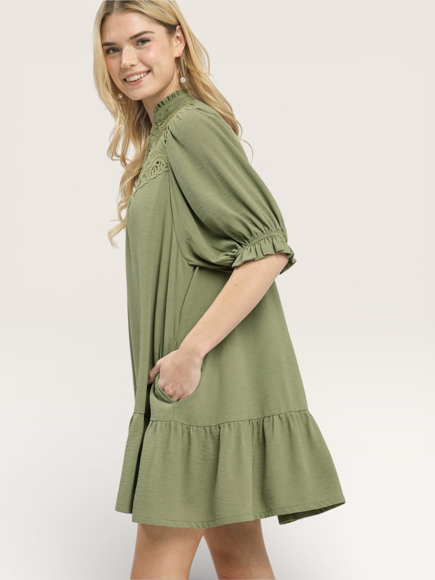 Woman wearing a green dress with long sleeves and a ruffled hem on a white background