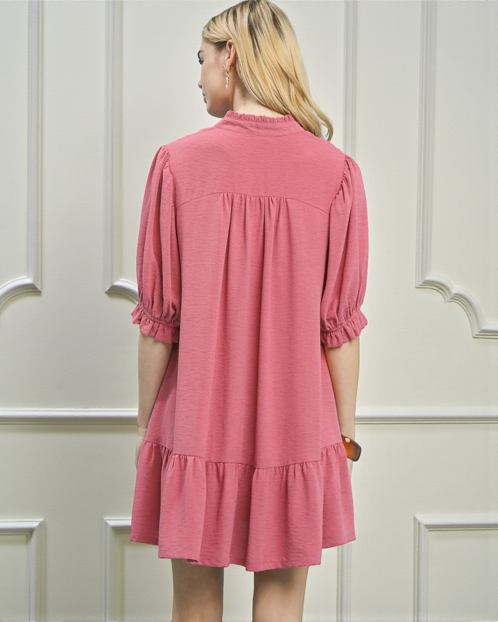 Woman wearing a pink dress against a white paneled wall