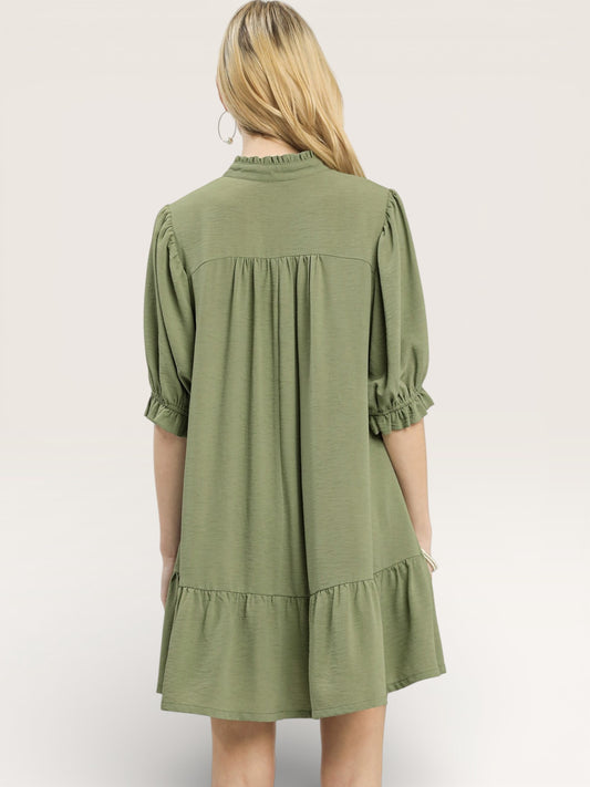 Woman wearing an olive green dress with a plain background