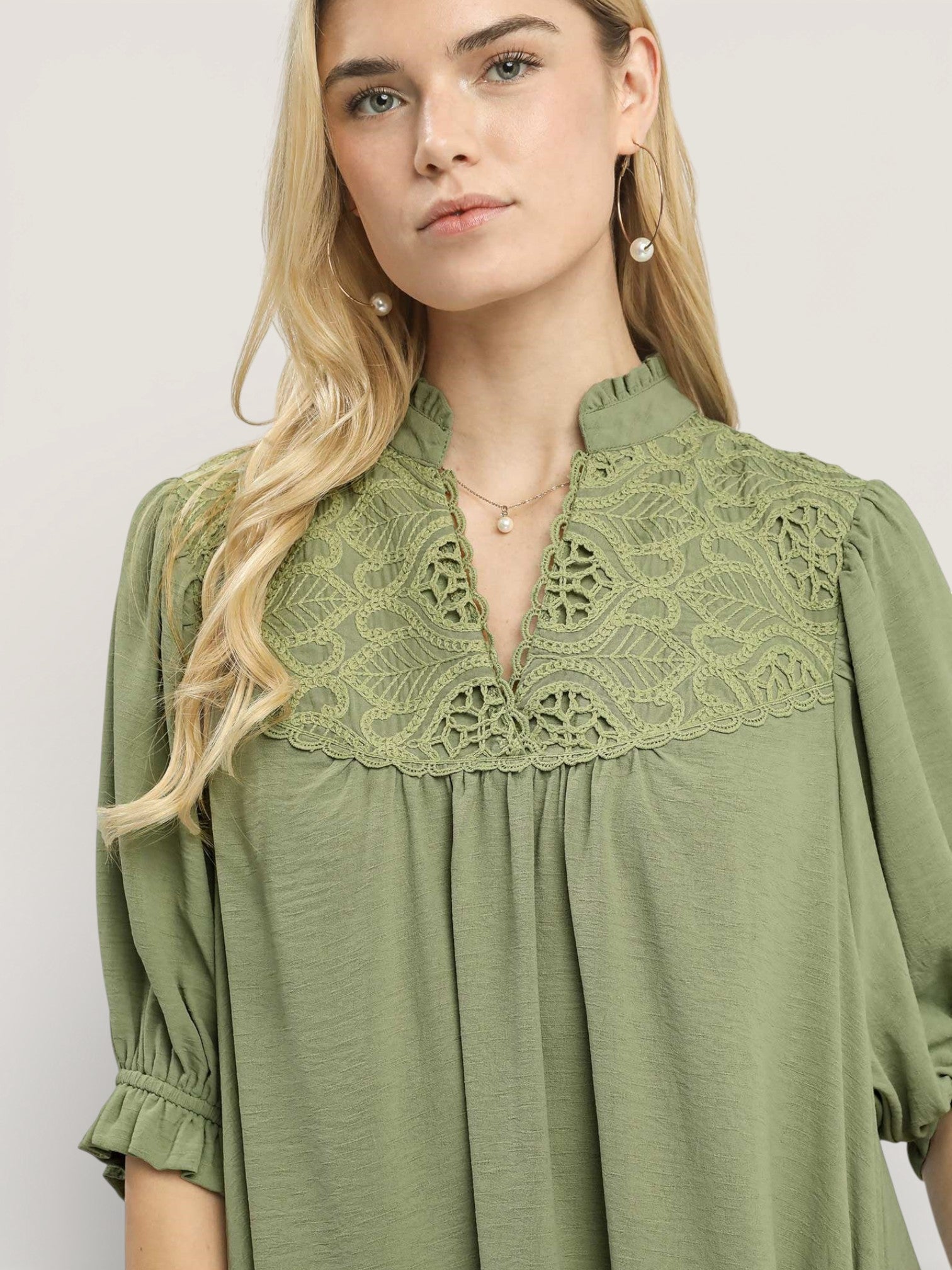 Woman wearing a green dress with lace neckline against a plain background