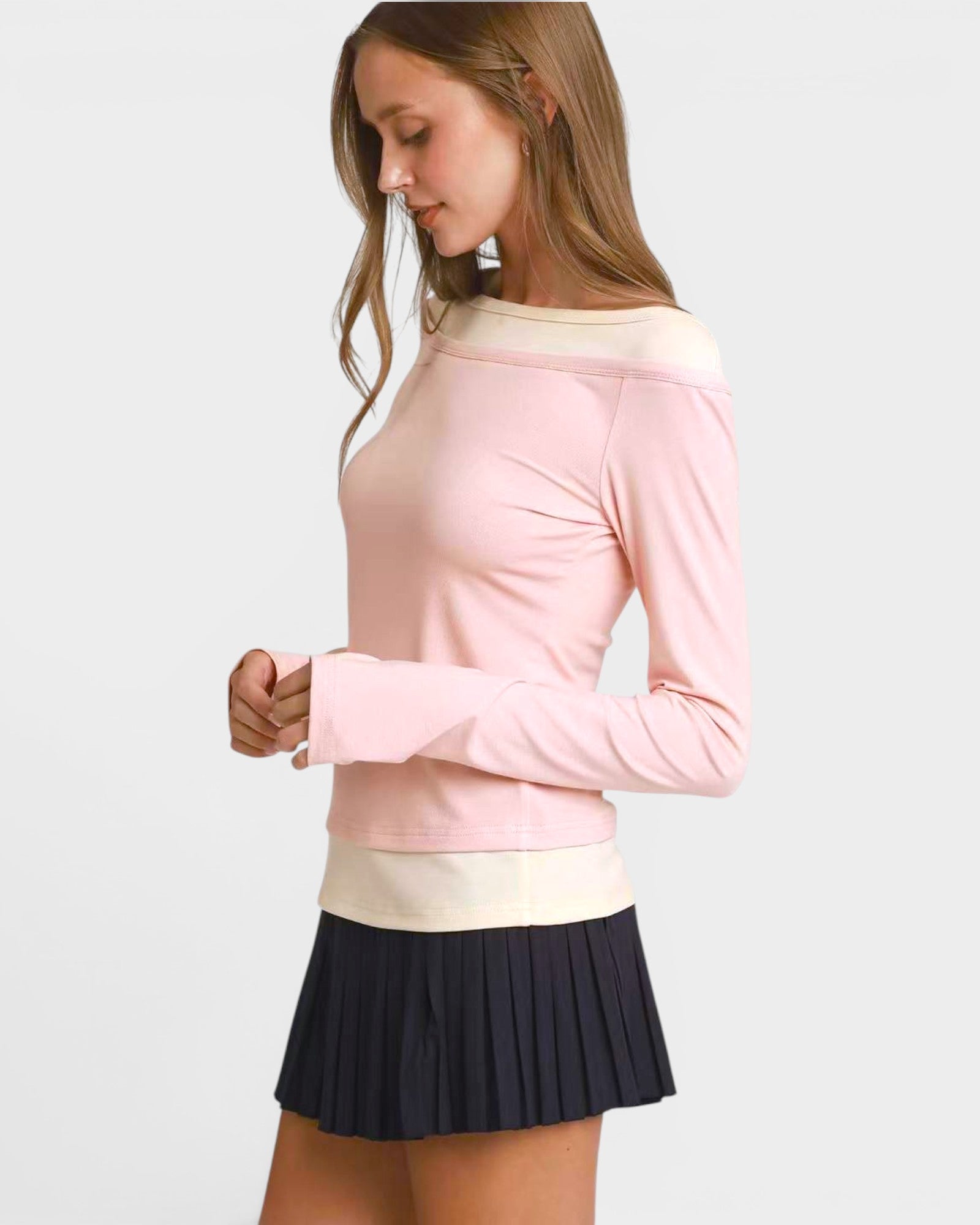 Woman wearing a pink long-sleeve top with a white collar and a pleated black skirt on a light gray background.