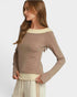 Woman wearing a brown long-sleeve top with a white trim on a light gray background