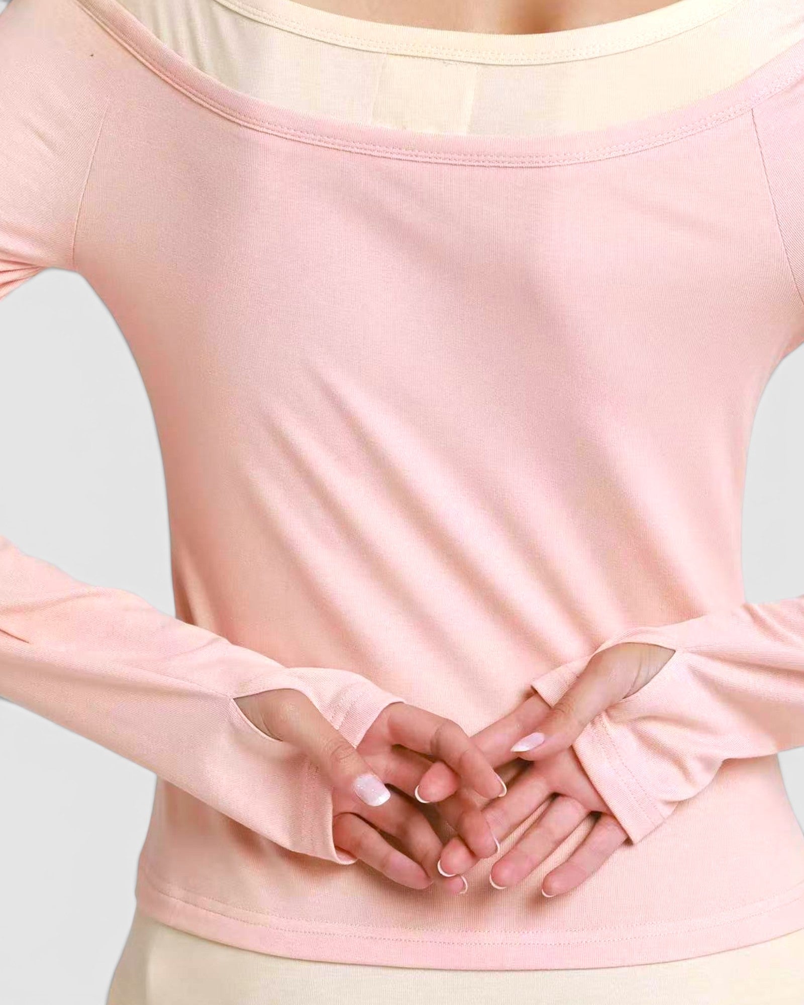 Person wearing a light pink long-sleeve top with a plain background