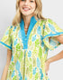 Woman wearing a colorful leaf-patterned shirt with blue accents on a plain background