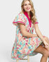 Woman wearing a colorful patterned dress sitting on a stool against a white background